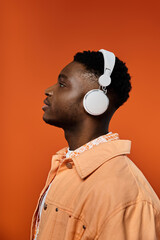 Fashionable young African American man enjoying music with headphones in front of bright orange...