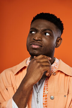 Handsome African American man in orange shirt, chin resting on hand.