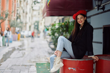 A beautiful woman smiling with teeth stands outside a cafe on a city street, a stylish fashion look of clothes, vacation and travel.
