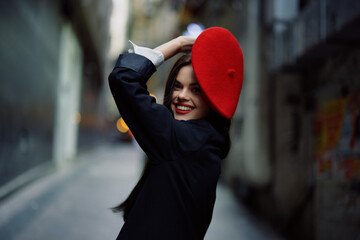 Fashion woman smile with teeth and fun tourist in stylish clothes in jacket and red beret walking down narrow city street flying hair, travel, French style, cinematic color, retro vintage style.