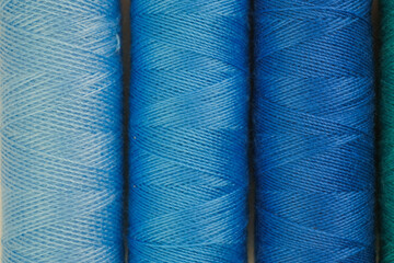 Collection of blue and green spools of thread neatly lined up in a row