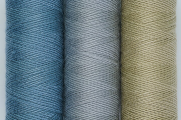 Three spools of thread in different colors, neatly lined up against a white background