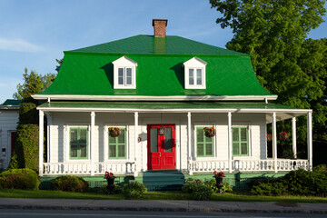 Beautiful second empire style white house with green metal mansard roof and red door seen during a...