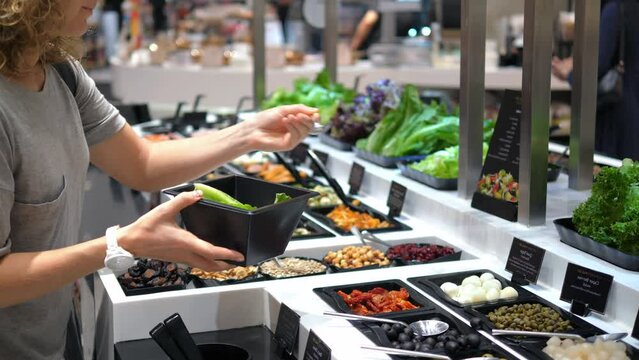 Woman selects ingredients for lunch at salad bar and puts them in her bowl. Quick lunch snack at supermarket with choice of fresh ingredients. Concept of choosing healthy foods for lunch.