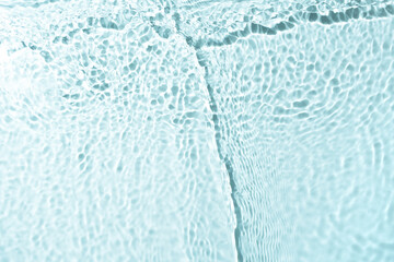 Close-up view of the surface of clear water formed by the interplay of light and ripples on water. Gentle waves create a mesmerizing texture, with circular ripples spreading out across the surface.
