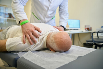Adult doctor massages the shoulders of an old patient