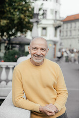 Smiling Senior Man in Yellow Sweater Leaning on Urban Balustrade