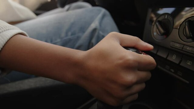 Close-up shot of hand of young African American lady wearing jeans sitting in car, driving, pressing on pedal and changing gears to start road trip