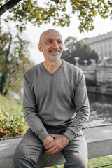 Elderly man sitting on a bench near a river, smiling and enjoying the day