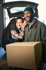 Young happy lady hugs a man holding a box in his hands near a car