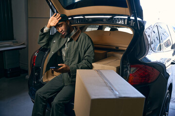 Young man sitting down to rest in the trunk of a car looking at his phone
