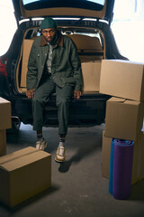 Fatigued young man sitting in the trunk of a automobile . Full length