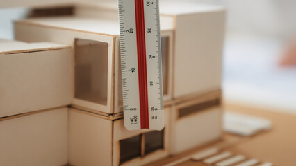 Closeup image of skilled professional engineer hand using ruler measures house model on table with...