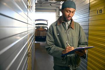 Young male writes in a folder while standing in a warehouse