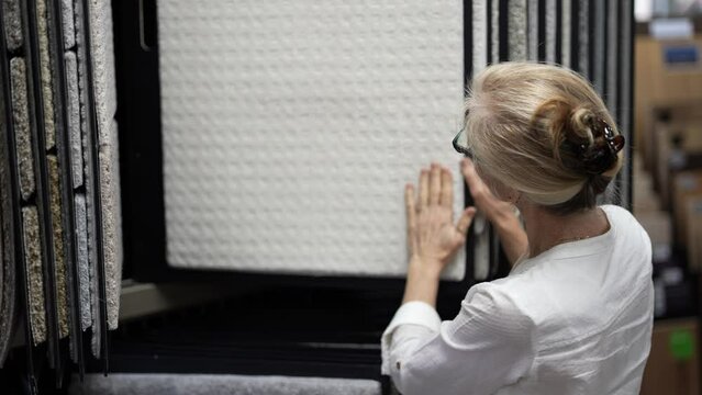 Happy mature woman touching carpet looking through samples for home redecorating project, in a floor store.