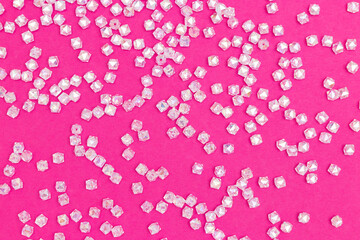 Texture made from transparent square acrylic beads scattered on a pink background.