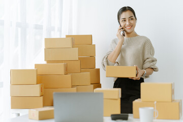 Starting small businesses SME owners asian female entrepreneurs call phone on receipt box and check online orders to prepare to pack the boxes, sell to