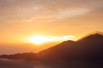 Sunrise over Mount Batur with a golden sky and silhouetted mountains. Travel