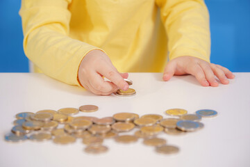 A girl collects and counts coins scattered on the table.