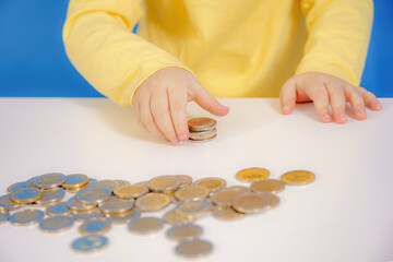 A girl collects and counts coins scattered on the table.