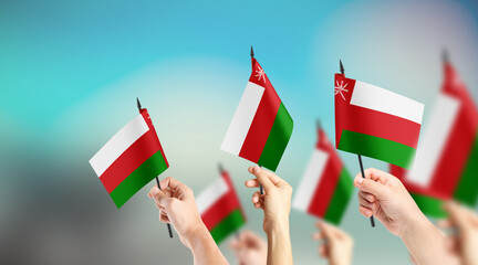 A group of people are holding small flags of Oman in their hands.