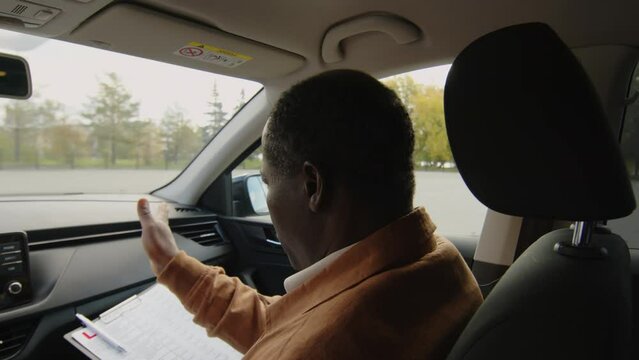 Back view of mature African American driving coach sitting in passengers seat of car, supervising offscreen learner motorist during training