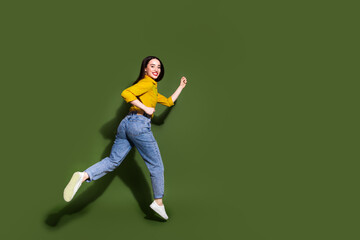 Full length photo of adorable lovely girl wear yellow shirt jumping high running empty space isolated green color background