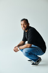 An African American man in a black shirt and jeans kneels down on a vibrant backdrop.