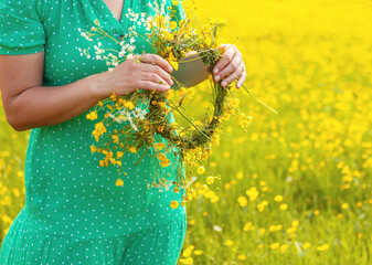 woman in green dress holds wreath of yellow flowers in the hands, crop, no face