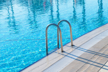 Swimming pool with stair and water. Swimming pool with handrail. Stainless steel ladder in pool. Grab bars ladder in the blue swimming pool