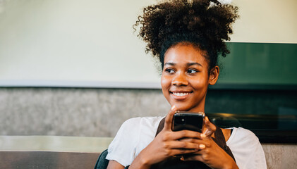 Close-up portrait of a black barista and coffee shop owner using a mobile phone. Smiling woman in...