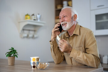 Cropped shot of a happy senior man standing alone in his living room at home and using his...