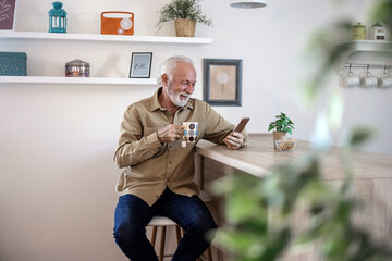 Mature man reading phone, social media notification and mobile app news in his kitchen home. Happy male drinking coffee, typing online smartphone and 5g wifi technology connection in house.