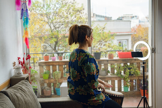 Rear view of unrecognizable Adult Woman at home calm in online drum class on the phone