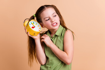 Photo of irritated kid girl look empty space listen loud bell clock isolated pastel color background