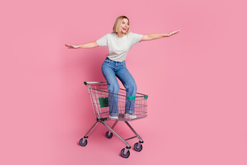 Photo of crazy cheerful girl wear trendy clothes riding in cart empty space isolated on pink color...