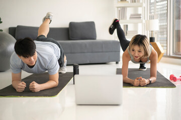 Contemporary young active couple in sportswear doing planks on the floor in front of laptop while...