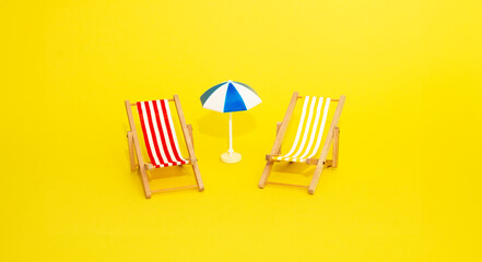 Beach relaxation and vacation concept. Toy sun lounger and umbrella on yellow colorful paper...