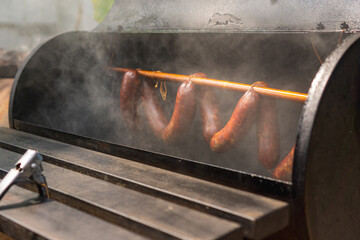 Smoked sausages hanging on rack in a offset smoker with a thick smoke, closed up