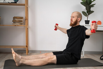 Concept of sport at home. Portrait of muscular young bearded man training with dumbbells at living...
