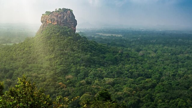 n aerial view of the iconic Sigiriya Rock Fortress rising above a vast, lush forest in Sri Lanka. The misty atmosphere and expansive greenery highlight the natural beauty and historical significance o