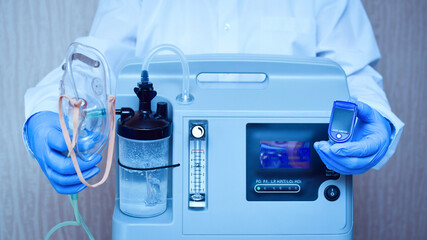 Hands in medical gloves hold an oxygen mask from the generator oxygen concentrator, which helps with low lung oxygen saturation, with pneumonia Covid-19 and pulse Oximeter in the other hand