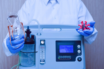 Hands in medical gloves hold an oxygen mask from the generator oxygen concentrator, which helps with low lung oxygen saturation, with Covid-19 pneumonia and coronavirus molecule model