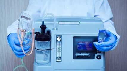Hands in medical gloves hold an oxygen mask from the generator oxygen concentrator, which helps with low lung oxygen saturation, with pneumonia Covid-19 and pulse Oximeter in the other hand