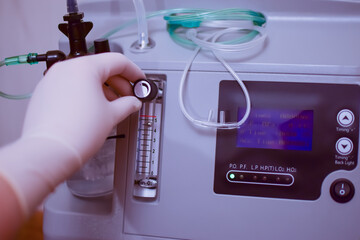 A hand in a medical glove regulates the supply of oxygen to the oxygen concentrator, which purifies...