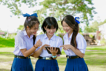 Group of Asian school girls teen friend in school uniform together look tablet happy smiling
