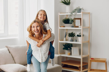 Mother and daughter laughing together in cozy living room with couch and bookshelves in the...