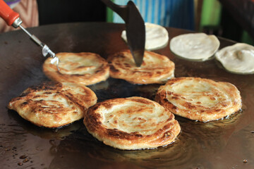 muslim vendor frying roti in flat pan on street food