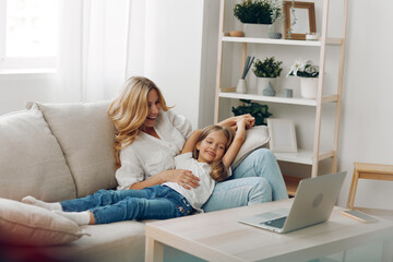 Mother and daughter bonding on the couch while looking at a laptop, smiling and enjoying quality time together