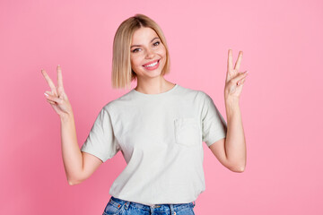 Portrait of cheerful optimistic girl with bob hairstyle wear white t-shirt showing v-sign symbol isolated on pink color background